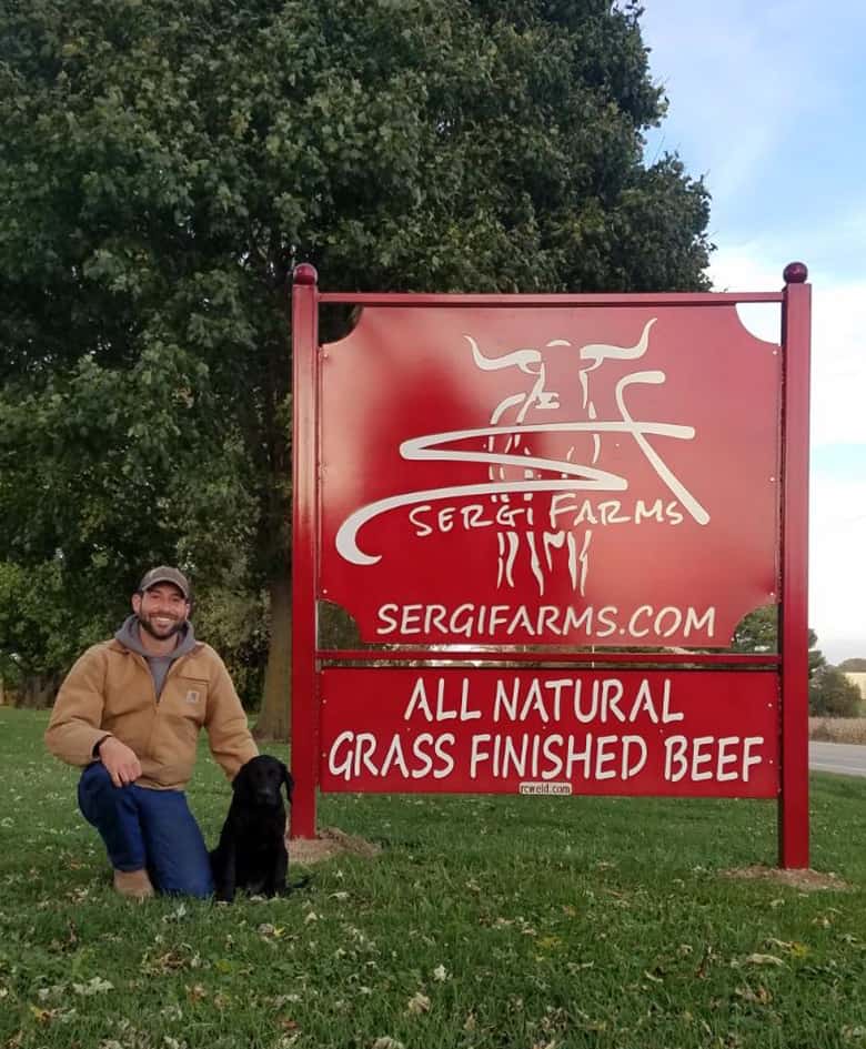 nick-with-sergi-farms-sign nick sergi in front of entrance sign